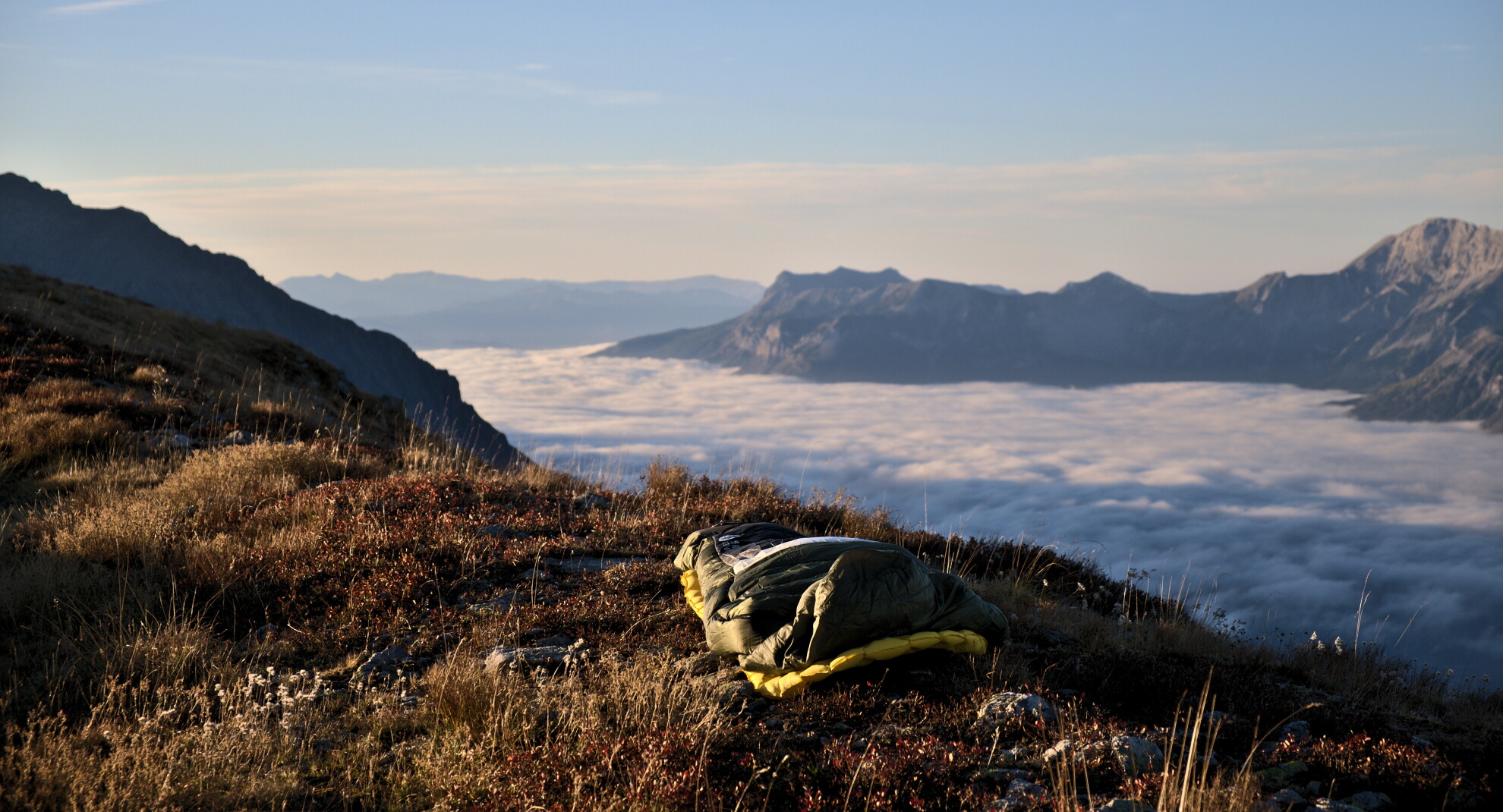 Saco de dormir sobre una loma herbosa por encima de un mar de nubes